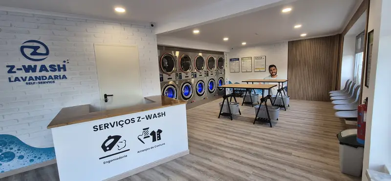 Interior da Z-WASH Odivelas: balcão de serviços, mesas e máquinas, com um cliente à espera